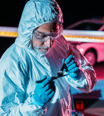 male criminologist in protective suit and latex gloves taking fingerprints from knife at crime scene